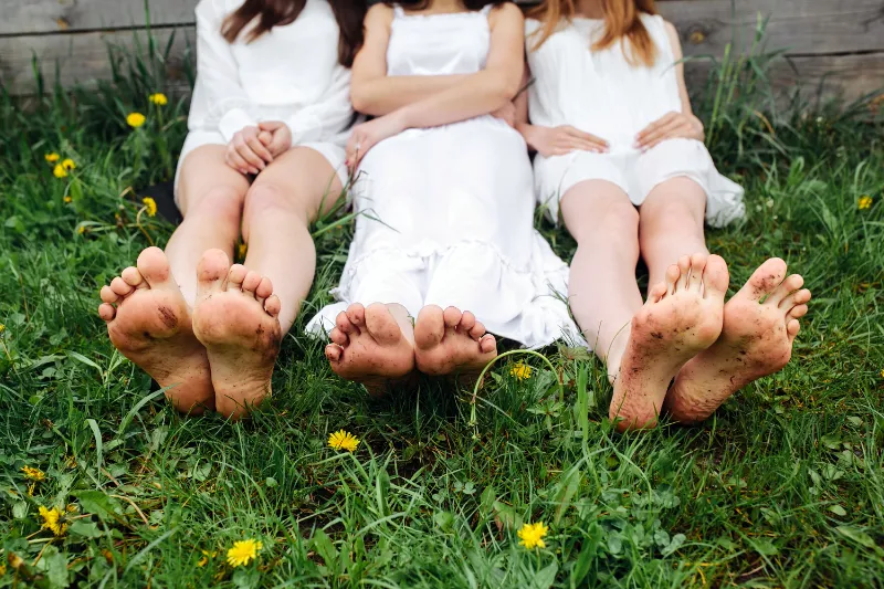 three pairs bare feet resting on green grass and dirt, symbolizing the practice of earthing